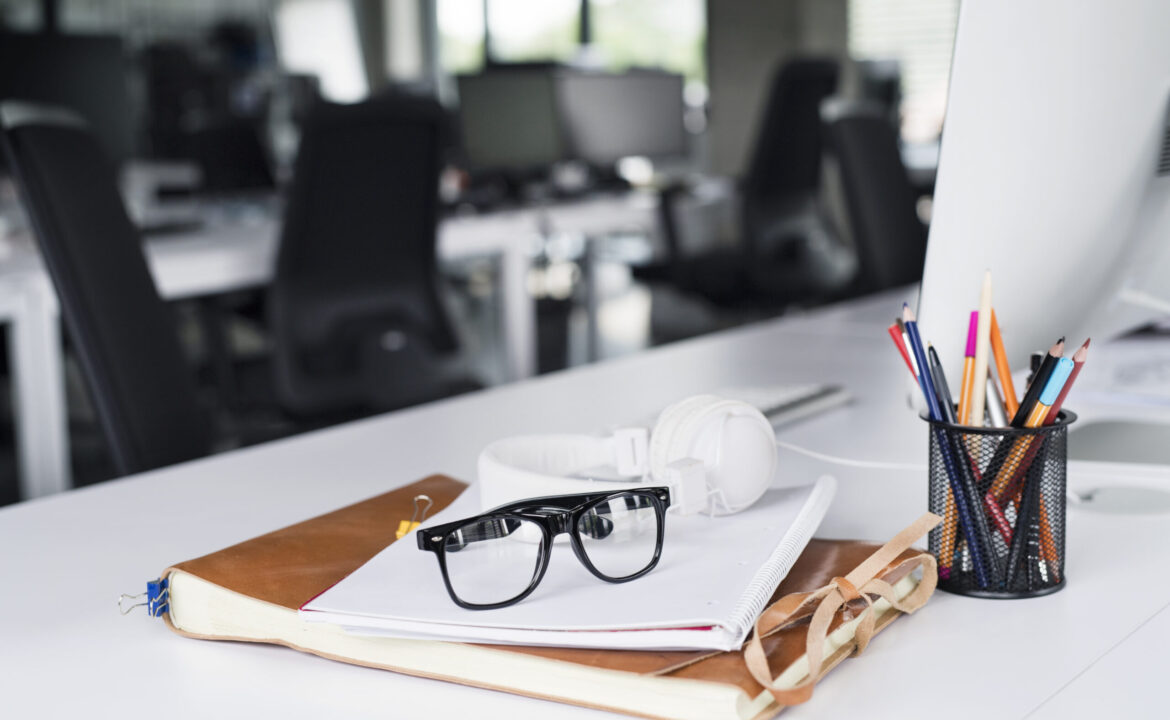 Office desk with computer, notebook and eyeglasses.